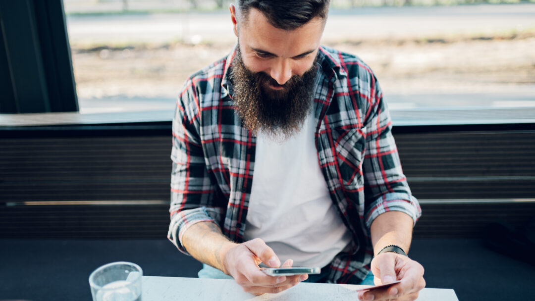 Bearded man using smartphone and a credit card in a cafe or restaurant