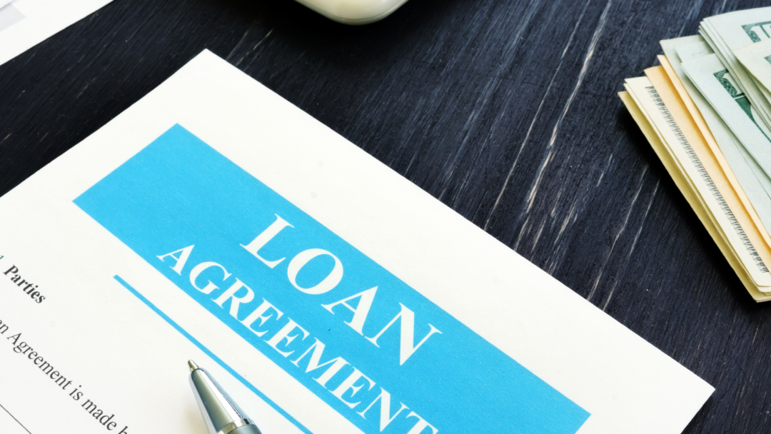 Close-up of a loan agreement document on a desk with a pen, cash, and calculator nearby.